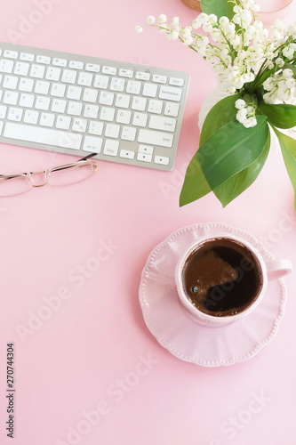 Pink flat lay top view women's office desk . Female workspace with laptop, white spring flowers lilies in a vase, accessories, notebooks mock up, glasses, cup of coffee on pale pink background. 