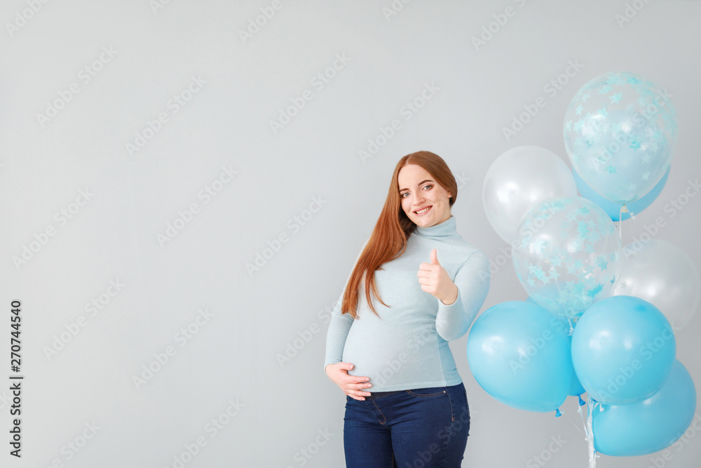 Beautiful pregnant woman with balloons showing thumb-up on light background Beautiful pregnant woman with balloons showing thumb-up on light background
