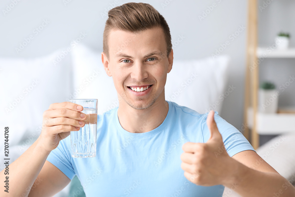 Handsome man with glass of water showing thumb-up at home Handsome man with glass of water showing thumb-up at home
