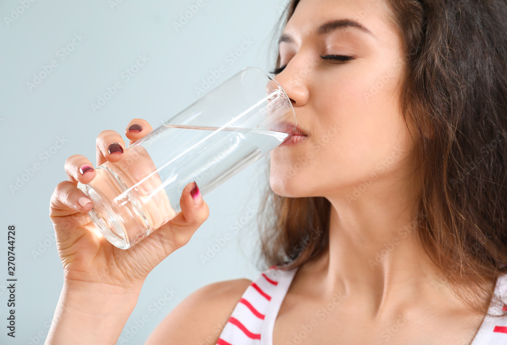 Beautiful young woman drinking water on light background Beautiful young woman drinking water on light background