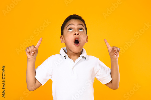 Portrait of cute little boy pointing at something on color background