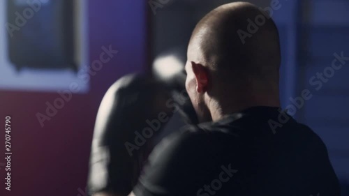 Backside view of boxer in boxing gloves makes punches in gym, slow motion