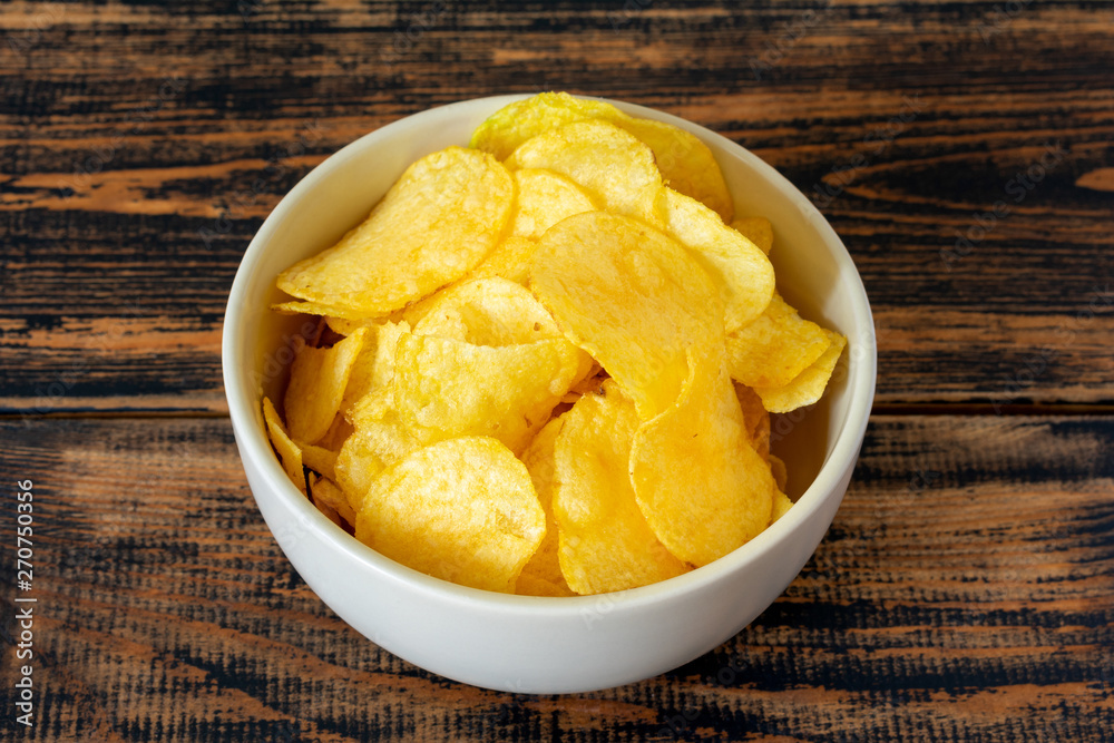 Golden potato chips on wooden background.