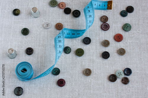 sewing tools: measuring tape, thimbles, small colored buttons scattered on a light gray background, selective focus