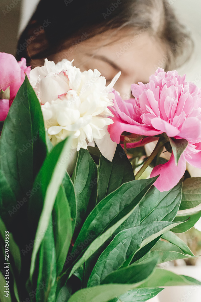 Girl holding and smelling beautiful pink and white peonies bouquet at rustic old wooden window. Floral decor and arrangement. Gathering flowers. Rural still life, countryside Girl holding and smelling beautiful pink and white peonies bouquet at rustic old wooden window. Floral decor and arrangement. Gathering flowers. Rural still life, countryside