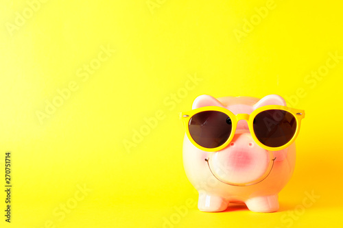 Happy piggy bank with sunglasses on yellow background, space for text. Finance, saving money