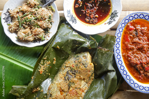 Traditional Indonesian cuisine. Grilled fish with spices served on the banana leaf with sauces and side dishes 