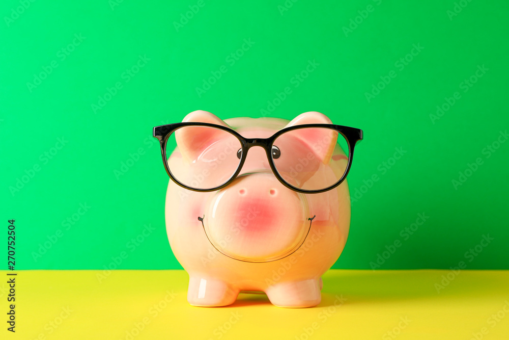Happy piggy bank with glasses on color table against green background, space for text. Finance, saving money Happy piggy bank with glasses on color table against green background, space for text. Finance, saving money