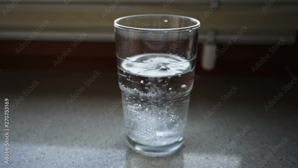 Throwing a tablet into a glass of water in slow motion while the tablet is dissolving in the water and sparkling Throwing a tablet into a glass of water in slow motion while the tablet is dissolving in the water and sparkling