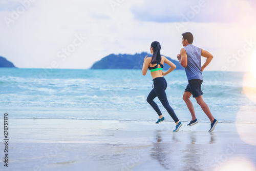 Couples runner jogging at the beach with sunset background.