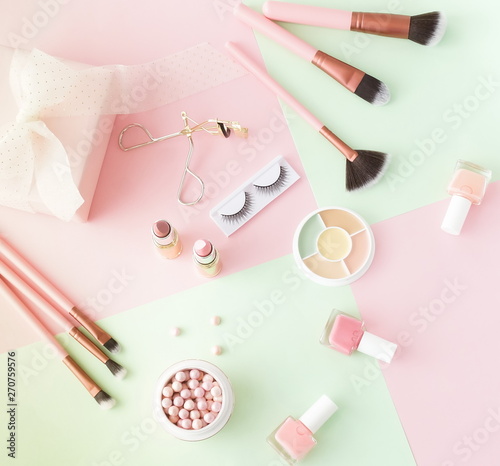 Makeup products, decorative cosmetics on pastel color pink mint background flat lay. Fashion and beauty concept. Top view. Copy space