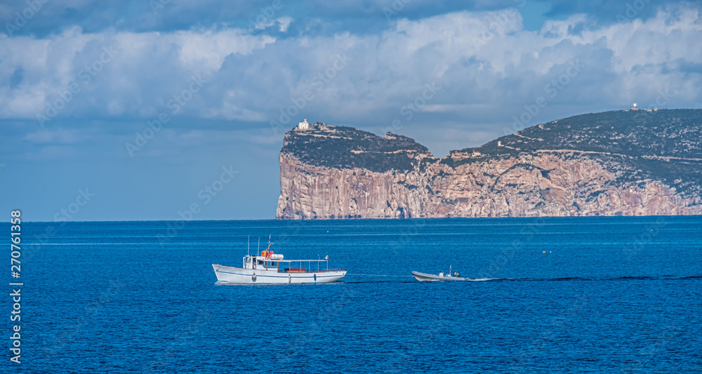 View of Capo Caccia from Alghero (L'Alguer),  as fishing boat entere the harbor, Sardinia, Italy.