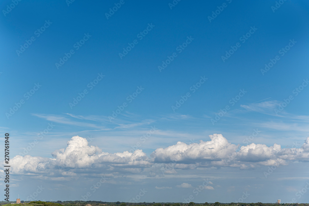 Obraz premium White clouds over the grass horizon and city skyline with a deep high altitude bleu spring sky