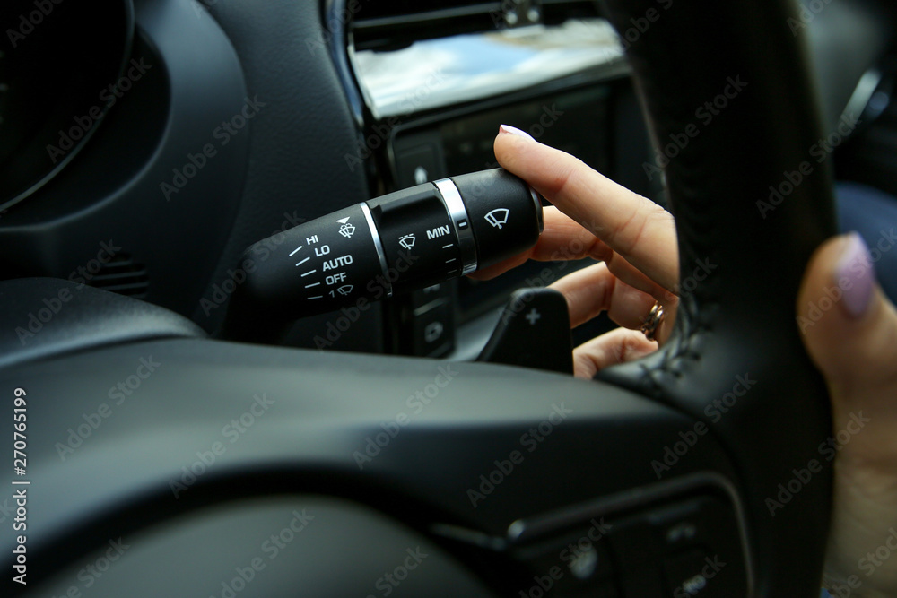 the hand of the driver switches the steering column switch. the hand of the woman turn on the wipers on the car close up