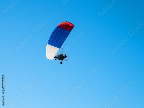 Colorful powered paraglider against blue sky.