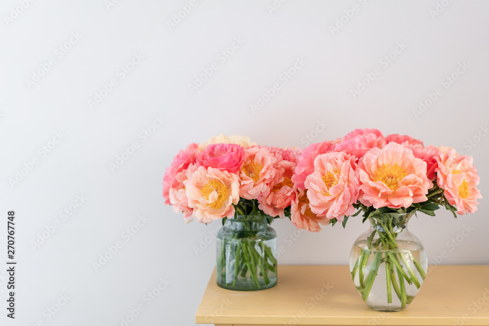 Cozy and atmosphere at home. Two glass vases with Coral peonies. Morning light in the room. Beautiful peony flower for catalog or online store. Floral shop and delivery concept .