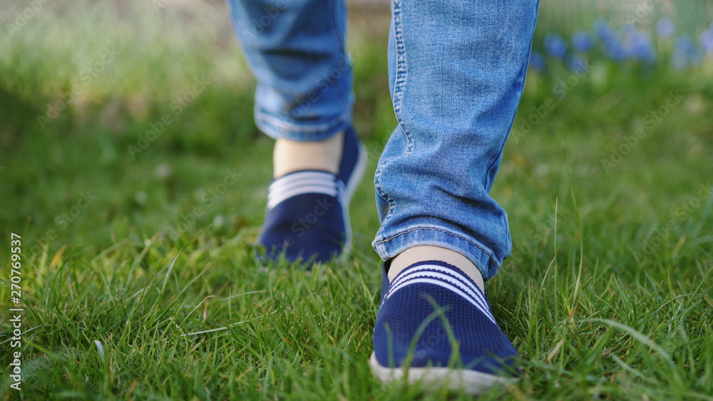 Young woman in blue sneakers goes on a meadow Young woman in blue sneakers goes on a meadow