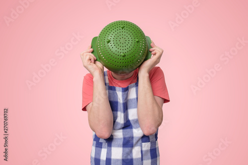 Man in apron holding colander near face hiding. photo