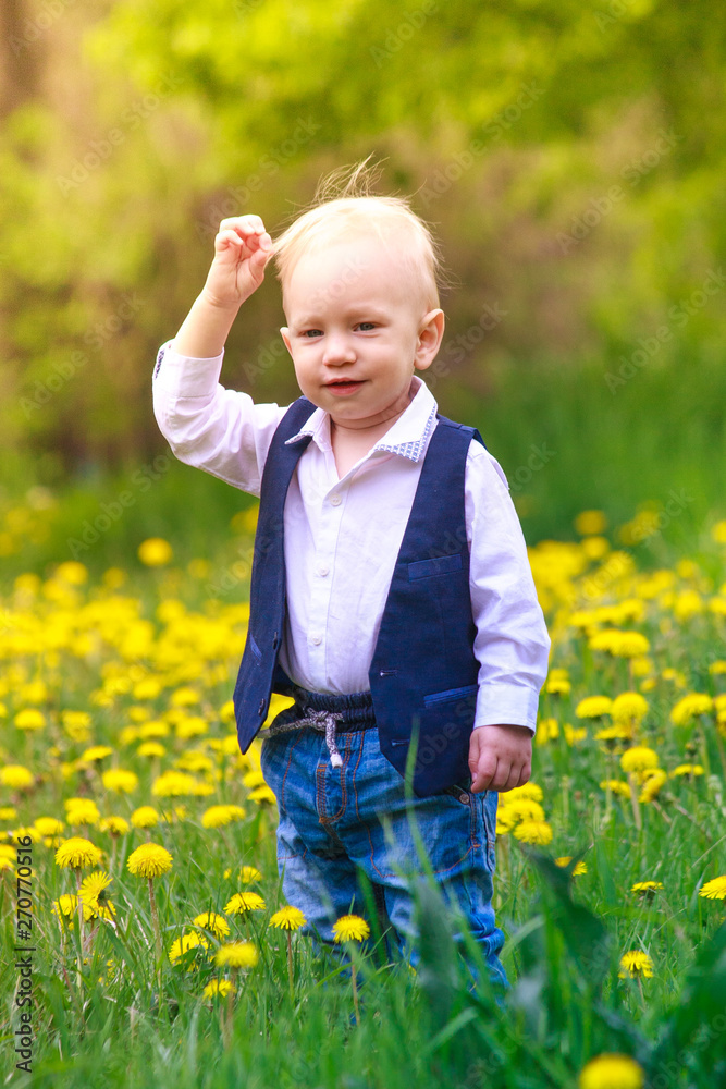 Toddler boy in a trendy stylish suit on a glade of blooming yellow dandelion flowers. series Emotions and laughter of a little boy. spring and bloom. Toddler boy in a trendy stylish suit on a glade of blooming yellow dandelion flowers. series Emotions and laughter of a little boy. spring and bloom.