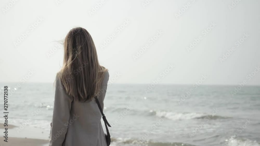 young happy woman with long hair in a beige coat close-up dancing on the sea beach young happy woman with long hair in a beige coat close-up dancing on the sea beach
