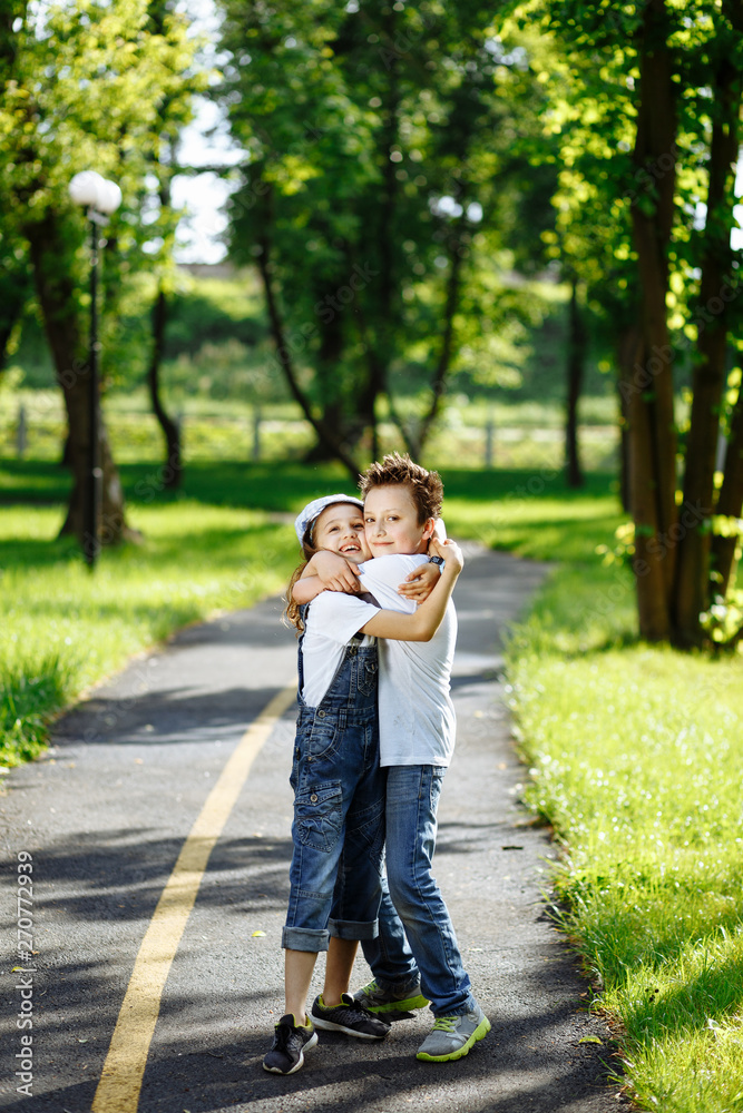 Obraz premium Picture of brother and sister having fun in the summer park on sunset. Cheerful children hugs and laughing. Little girl and boy playing outdoors, best friends, happy family, love and happiness concept