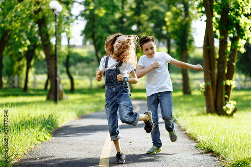 Fototapeta Naklejka Na Ścianę i Meble -  Brother and sister running in the summer park on sunset. Cheerful children. Little girl and boy are doing sports outdoors, best friends. Childhood concept