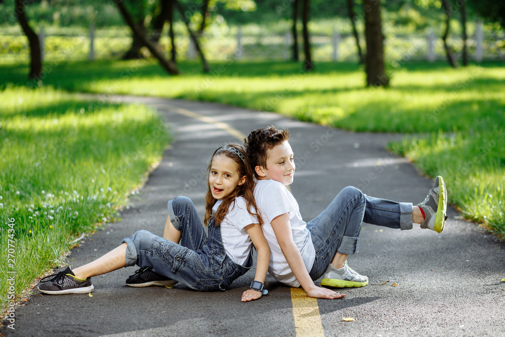 Brother and sister play on the ground in the summer park on sunset. Cheerful children. Little girl and boy outdoors, best friends. Childhood concept Brother and sister play on the ground in the summer park on sunset. Cheerful children. Little girl and boy outdoors, best friends. Childhood concept
