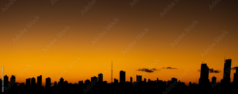 Fototapeta premium Zachód słońca w mieście, kiedy pomarańczowe niebo kontrastuje z budynkami prostymi liniami.