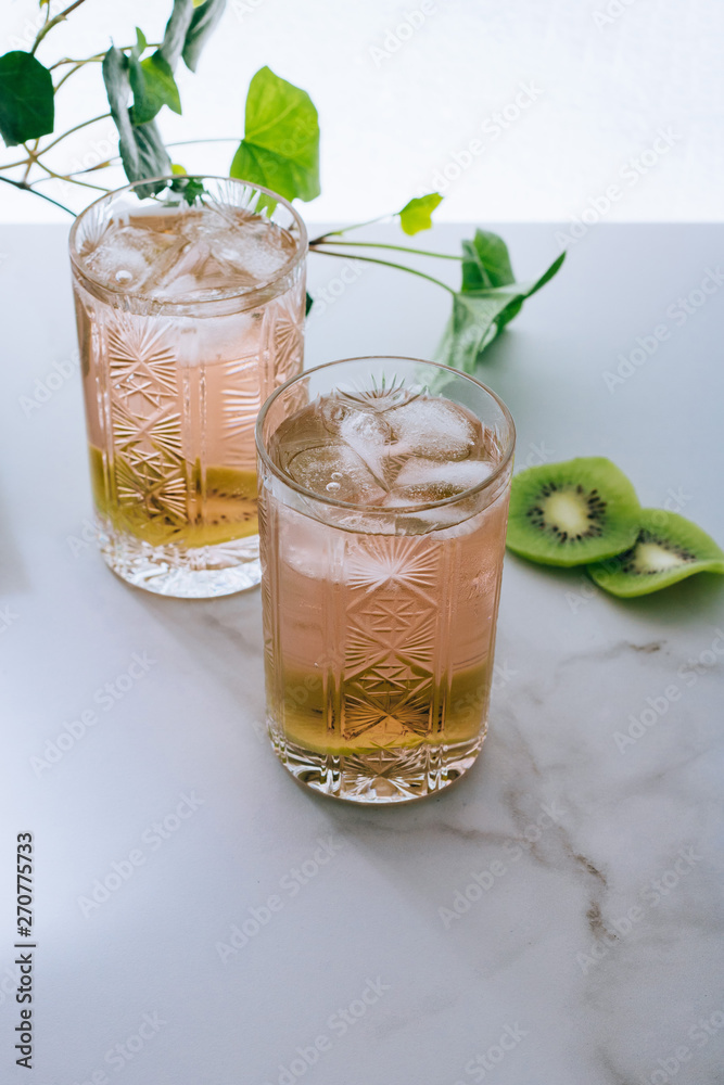Fototapeta premium A glass of pink wine in a crystal glass on a marble background, green ivy and bright sun
