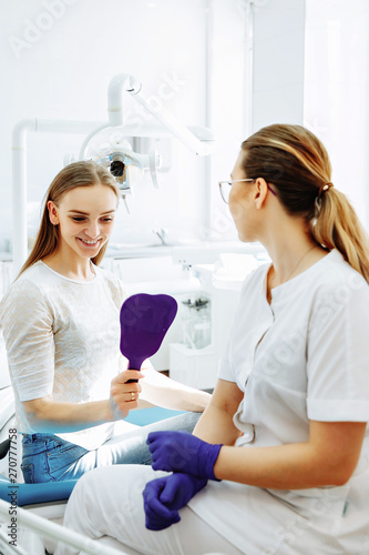 A woman is sitting at a dentist's reception. She looks in the mirror at her teeth.