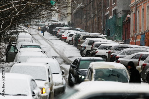 Cars drive along a snowy road in the snowfall in winter. Road traffic in the winter season.