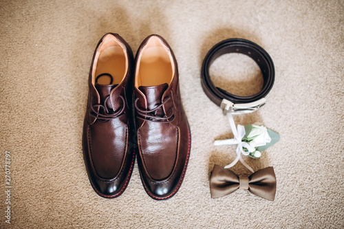 Men's accessories, leather belt, perfume, bow tie, groom's golden rings, watches and brides on a white table. Businessman clothing detail concept