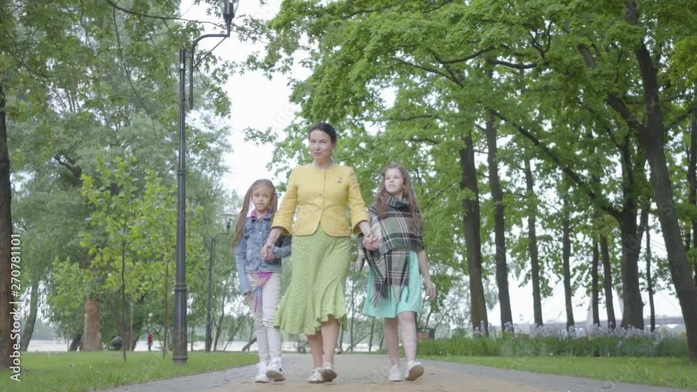 Mature elegant woman walking in the park with her two granddaughters. Happy family holding hands. Grandmother spending time with grandkids outdoors. Concept of generations. Leisure together. Mature elegant woman walking in the park with her two granddaughters. Happy family holding hands. Grandmother spending time with grandkids outdoors. Concept of generations. Leisure together.