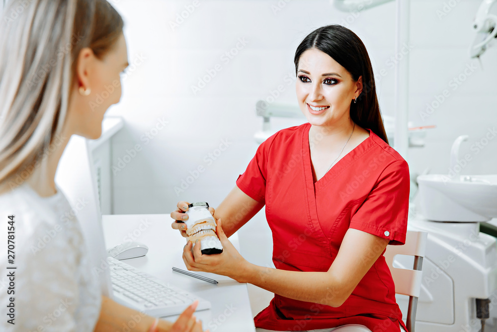 Obraz premium Concentrated dentist sitting at table and shows jaw samples tooth model to the patient