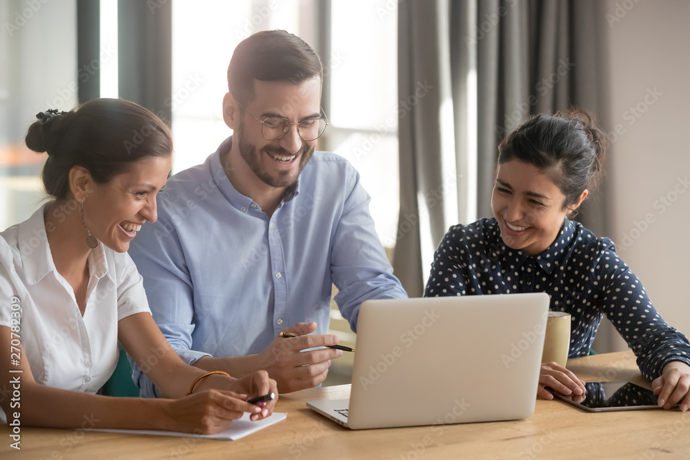 Smiling diverse employees watch funny video at laptop