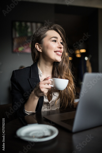 Portrait of a young beautiful businesswomen enjoying coffee during work on portable laptop.
