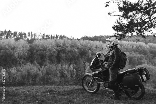 Rider standing with adventure motorcycle  Motorcyclist gear  A motorbike driver  concept of active lifestyle  enduro travel road trip. Evening  autumn. Tourist traveler. copy space  black and white