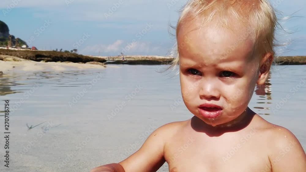 portert is a two-year-old blond boy at sea. on the face of the child played the reflection of the sun from the water. slow motion. portert is a two-year-old blond boy at sea. on the face of the child played the reflection of the sun from the water. slow motion.