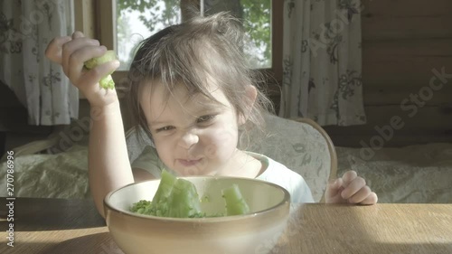 Happy little girl hate eating broccoli vegetables on a plate with hands