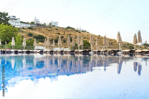 Outdoor luxury swimming pool, umbrellas, sun beds with reflection in the water at the holiday, background is beautiful mountain, relax place. © YuliiaMazurkevych
