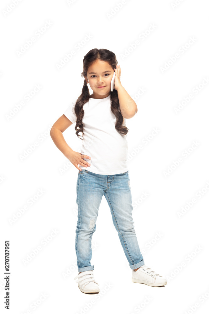 happy latin kid standing with hand on hip and talking on smartphone isolated on white happy latin kid standing with hand on hip and talking on smartphone isolated on white
