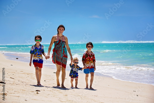 Happy beautiful fashion family, mom and children, dressed in hawaiian shirts, playing together on the beach © Tomsickova