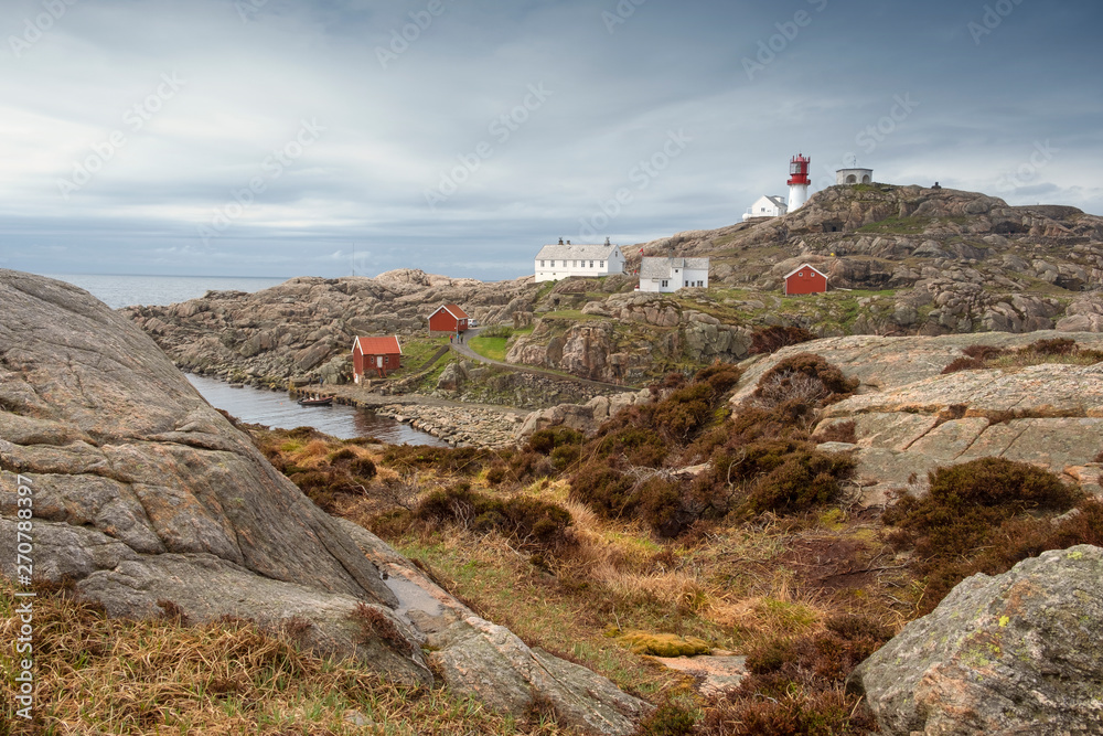 Norway in the spring. landscape rocky coast of the northern sea, traditional wooden red Norwegian houses and the southern lighthouse Lindesnes fyr