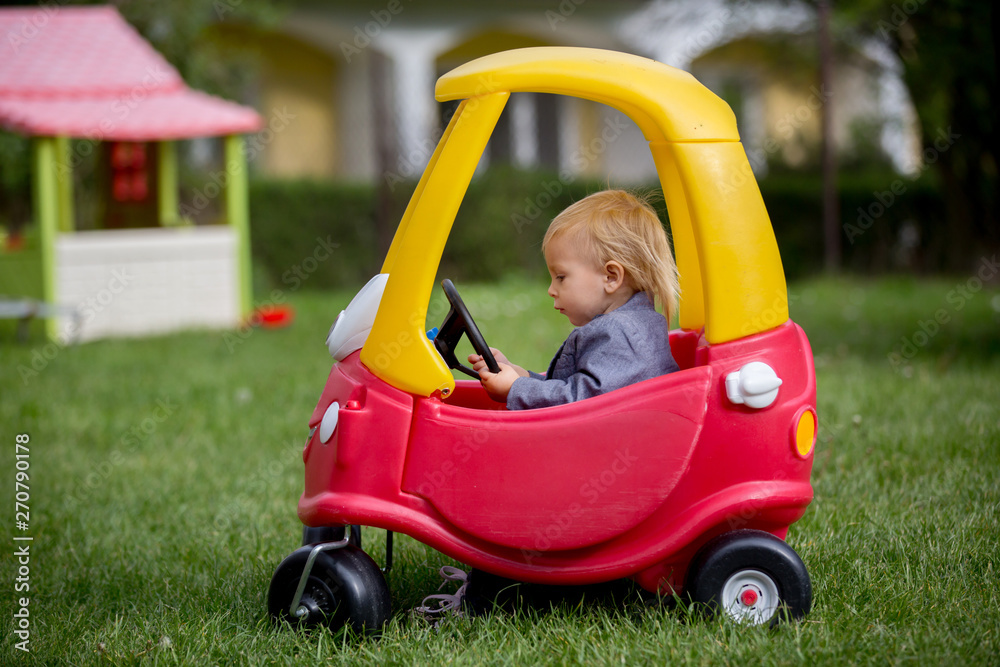 Cute toddler boy, riding big plastic red car toy in the park Cute toddler boy, riding big plastic red car toy in the park