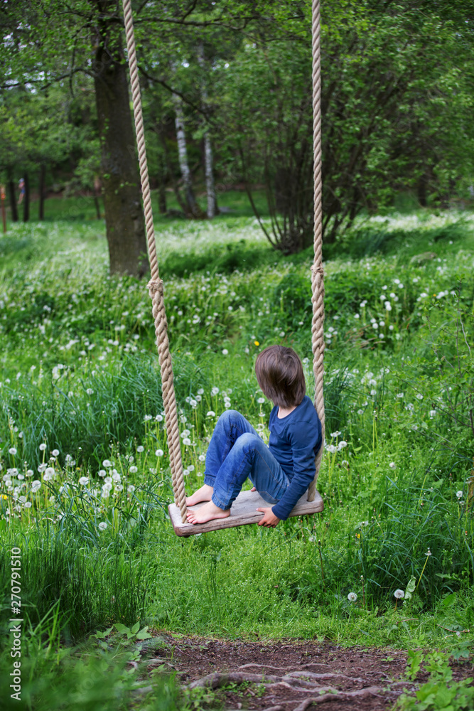 Sweet child, preteen boy, swinging on a wooden swing