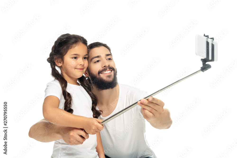 happy kid holding selfie stick while taking selfie with latin father isolated on white