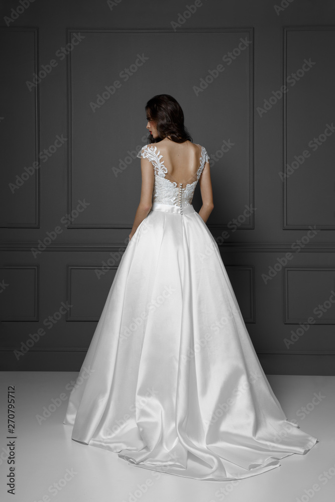 Back view of a tender brunette model in white delicate princess wedding dress, isolated on a grey background. Back view of a tender brunette model in white delicate princess wedding dress, isolated on a grey background.