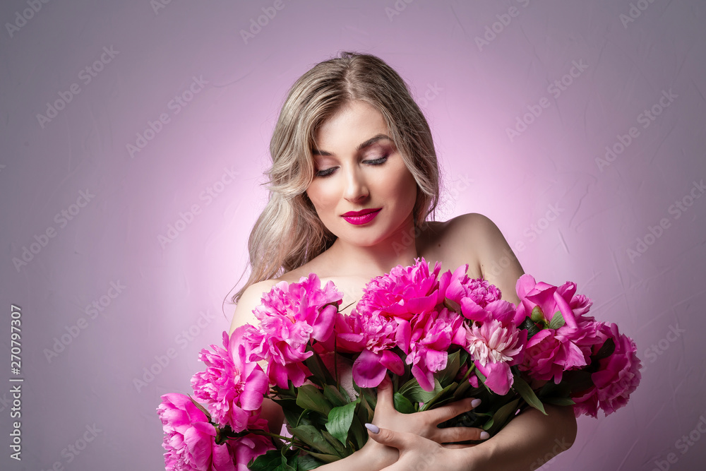 Close up portrait of an attractive young woman holding flowers pions bouquet on pink background. Female fashion concept. space for text