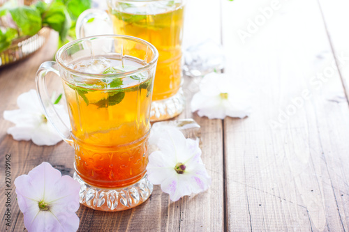 Black iced tea with lemon and mint in glass cups on a wooden table, horizontal, copy space