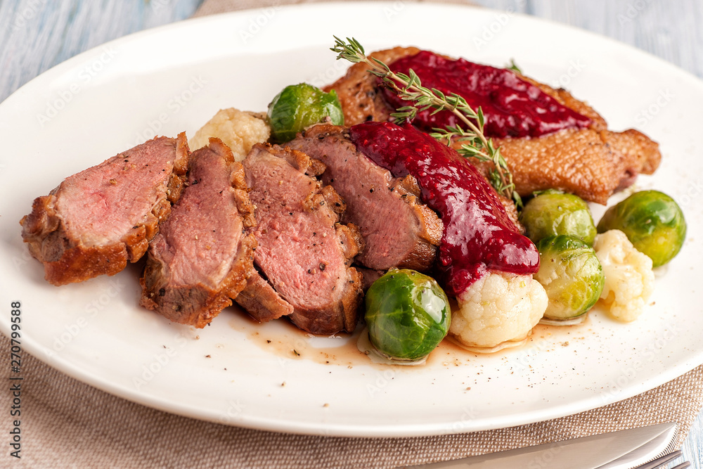 Roasted duck breast with vegetable garnish. The meat is sliced into portions and sprinkled with cranberry berry sauce. Large portion on a plate. Close up and horizontal view. Roasted duck breast with vegetable garnish. The meat is sliced into portions and sprinkled with cranberry berry sauce. Large portion on a plate. Close up and horizontal view.
